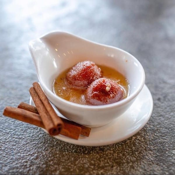 Two Gulab Jamun in syrup, garnished with cinnamon sticks, on a white dish.