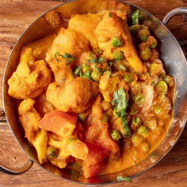 Aloo Gobi, an Indian dish with cauliflower, potatoes, and peas in a rich orange sauce.